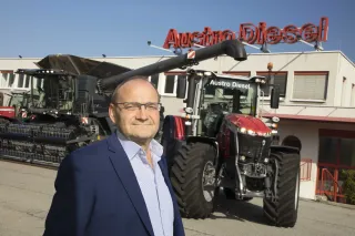 Muž stojí před traktorem Massey Ferguson a budovou Austro Diesel.