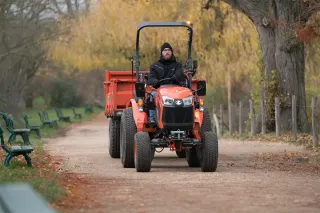 Řidič na oranžovém malotraktoru Kubota s přívěsem.