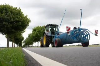 Traktor převáží modrý prstencový pěch Lemken po silnici.