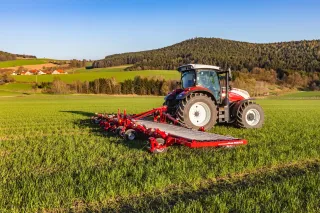 Traktor s červenými prutovými branami Horsch na louce.