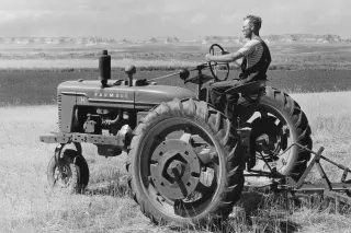 Historická černobílá fotografie traktoru Farmall s řidičem na poli.