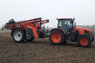 Traktor Kubota s taženým postřikovačem na poli.