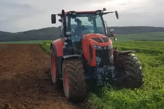 Oranžový traktor Kubota na okraji pole.