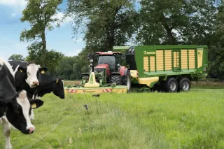 Traktor se žacím strojem Krone a sběracím vozem na louce s kravami.
