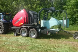 Traktor s lisem Kverneland a ovinutým kulatým balíkem na louce.
