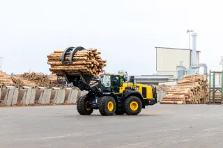 Kolový nakladač Komatsu převáží klády v areálu.