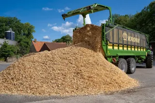 Zelený přepravní vůz Krone vysypává řezanku.