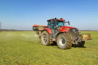 Červený traktor Case IH s rozmetadlem na poli.