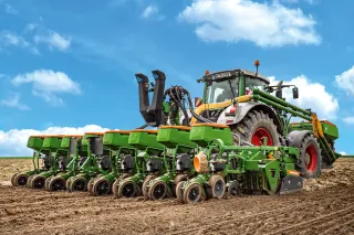 Traktor se zeleným secím strojem Amazone na poli.