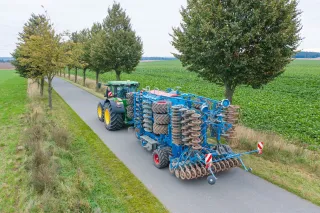 Traktor převáží složený modrý secí stroj Lemken po silnici.