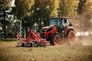 Oranžový traktor Kioti s nářadím na poli.