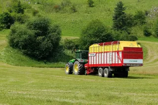 Traktor se sběracím vozem Pöttinger na louce.