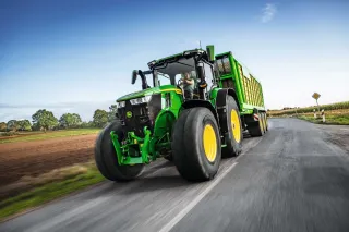 Zelený traktor John Deere s vozem na silnici.