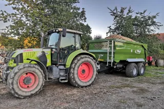 Traktor Claas se zeleným návěsem Fliegl na dvoře farmy