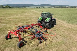 Traktor s červeným rotorovým shrnovačem ROZMITAL na louce