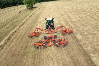 Traktor se čtyřrotorovým shrnovačem Kuhn při práci na louce