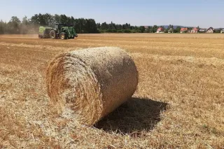 Kulatý balík slámy na poli se strojem v pozadí