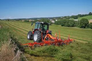 Traktor s oranžovým obracečem Kuhn na louce
