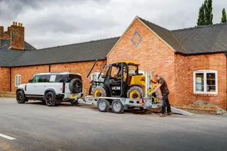 Malý žlutý manipulátor JCB na přívěsu za bílým automobilem