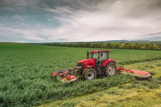 Červený traktor s žacími stroji při sečení zeleného porostu