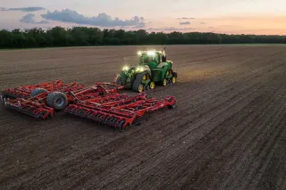 Traktor s červeným kypřičem Kuhn Prolander na poli za soumraku