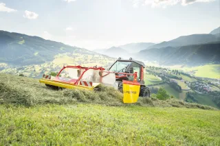 Traktor s pásovým shrnovačem Pöttinger na horské louce