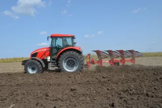 Červený traktor s pluhem SUKOV při orbě