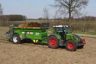 Traktor se zeleným rozmetadlem hnoje HAWE na poli