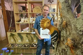 Muž s listinou stojí vedle modelu ptáka a stromu