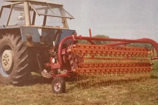 Historický snímek traktoru s červeným shrnovačem na louce