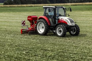 Červenobílý traktor Steyr se secím strojem na louce