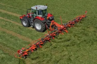 Traktor s širokým obracečem Kuhn při práci na louce