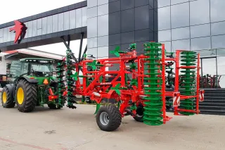 Traktor s červenozeleným kypřičem AGRO-MASZ před budovou