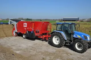 Modrý traktor s červeným krmným vozem BvL na farmě