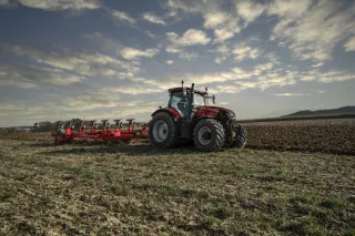 Červený traktor Case IH Puma s připojeným nářadím na poli