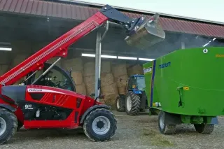 Červený teleskopický manipulátor Faresin zvedá lopatu u krmného vozu