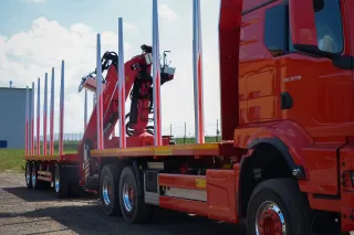 Červený nákladní automobil s přívěsem pro přepravu dřeva