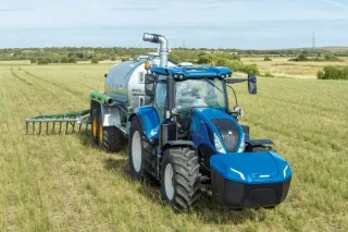 Modrý traktor New Holland s cisternou na poli