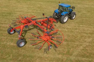 Modrý traktor s červeným shrnovačem Kuhn na louce