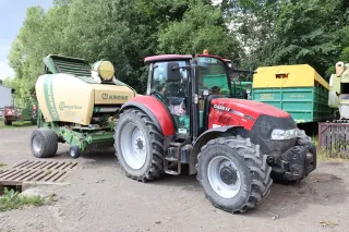 Červený traktor Case IH s lisem Krone na farmě
