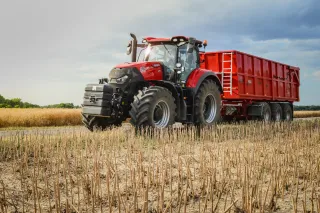 Červený traktor s červeným zemědělským návěsem na poli