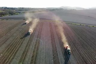 Tři zemědělské stroje John Deere při práci na poli z ptačí perspektivy