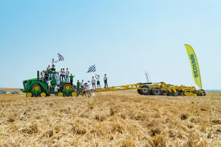 Pásový traktor táhne žlutý podmítač BEDNAR, lidé oslavují rekord na poli