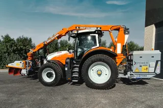Oranžový komunální traktor Steyr s připojeným nářadím