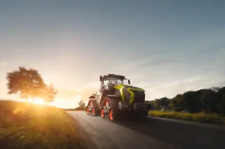 Traktor CLAAS XERION s pásovými jednotkami jede po silnici za soumraku
