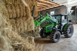 Zelený traktor Deutz-Fahr s čelním nakladačem u stohu balíků