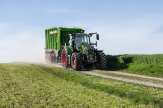 Zelený traktor Fendt s návěsem jede po polní cestě