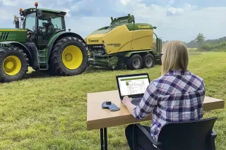 Žena s notebookem sleduje traktor a lis Krone při práci na poli