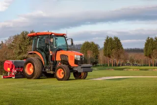 Oranžový komunální traktor Kubota při práci na trávníku