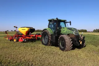 Tmavý prototyp traktoru Steyr Hybrid CVT s červeným secím strojem na poli.